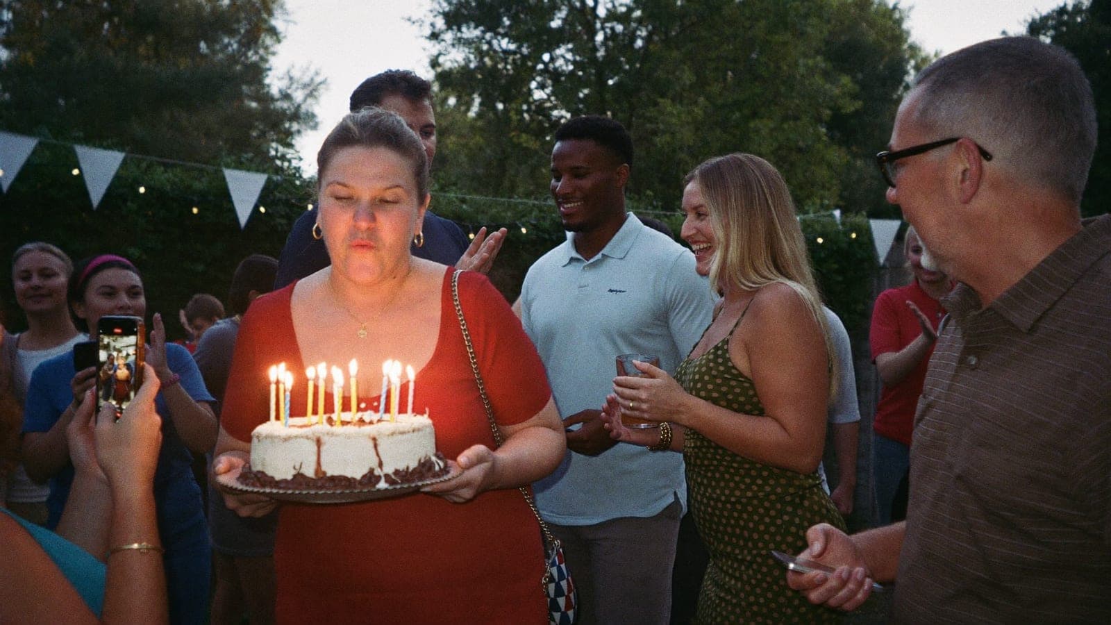 Een vrouw blaast op haar vijftigste verjaardag de kaarsjes uit terwijl vrienden en familie juichen