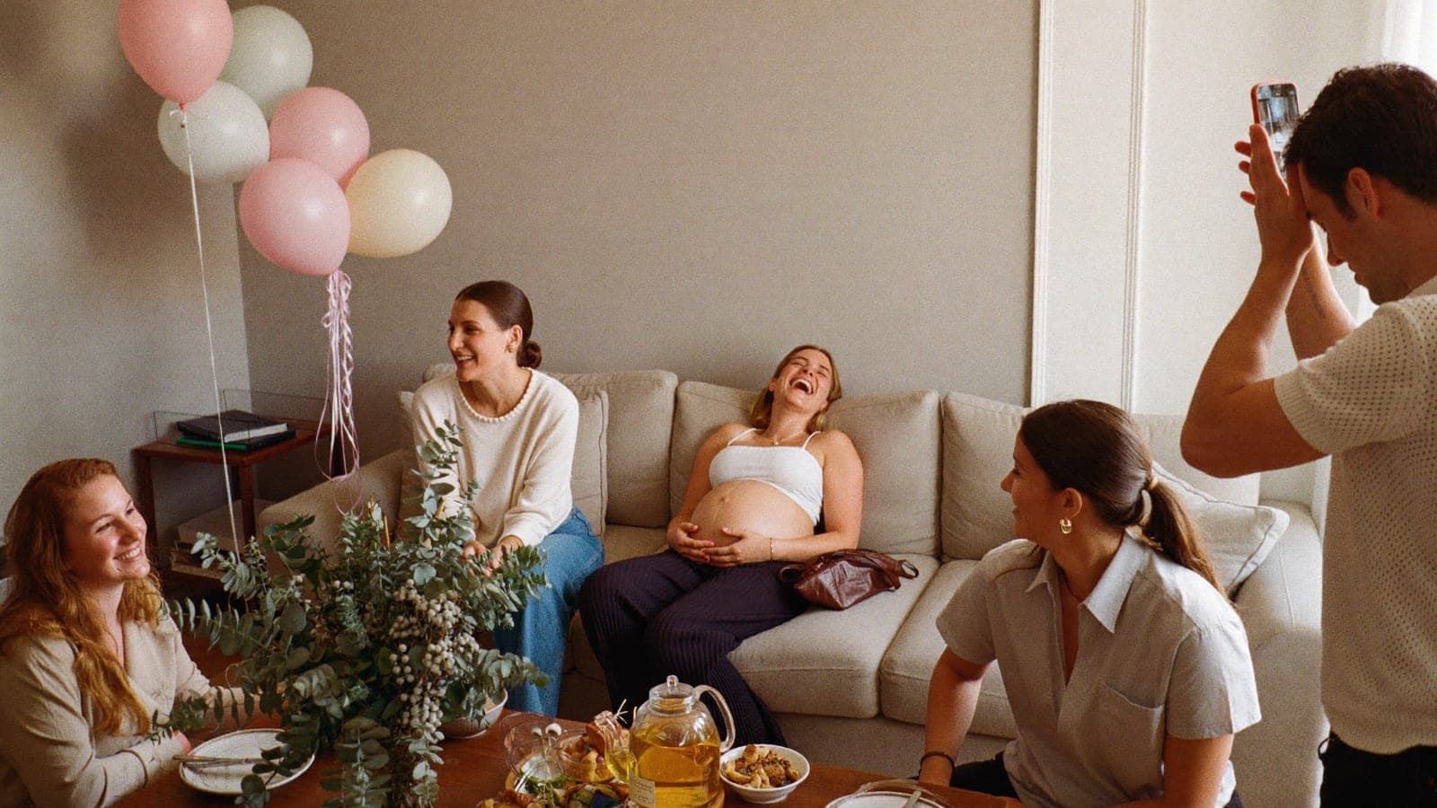 Een zwangere vrouw lacht op de bank tussen haar vriendinnen tijdens de babyshower met high tea
