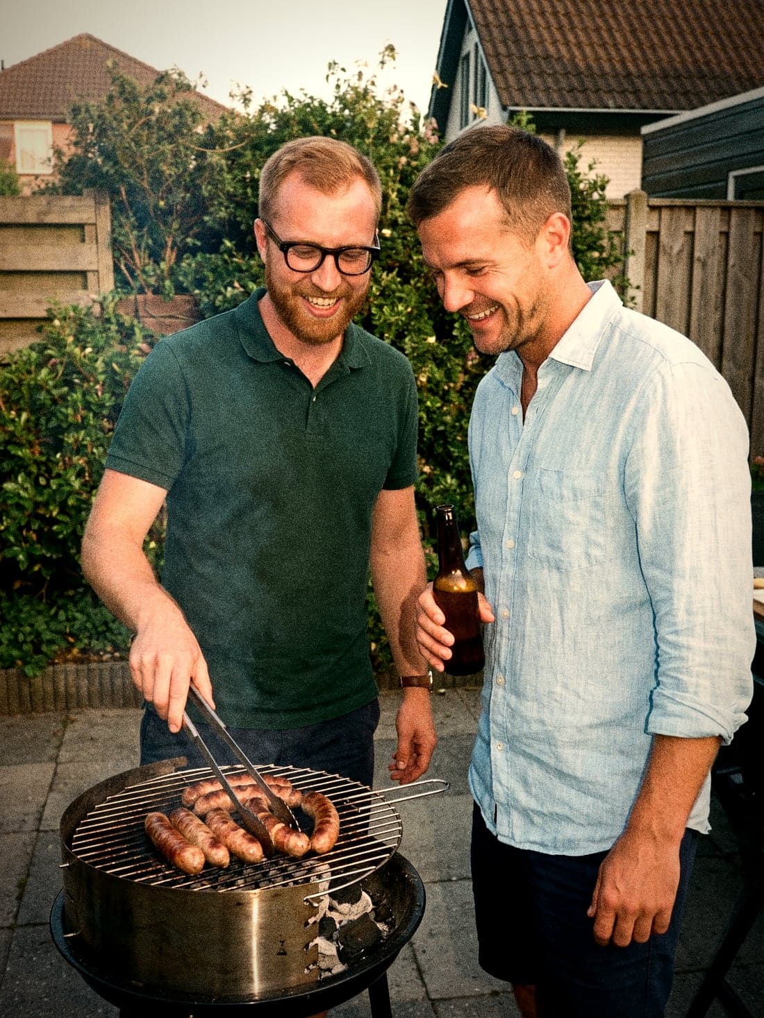 Joost staat aan de barbecue, Mark kijkt lachend mee