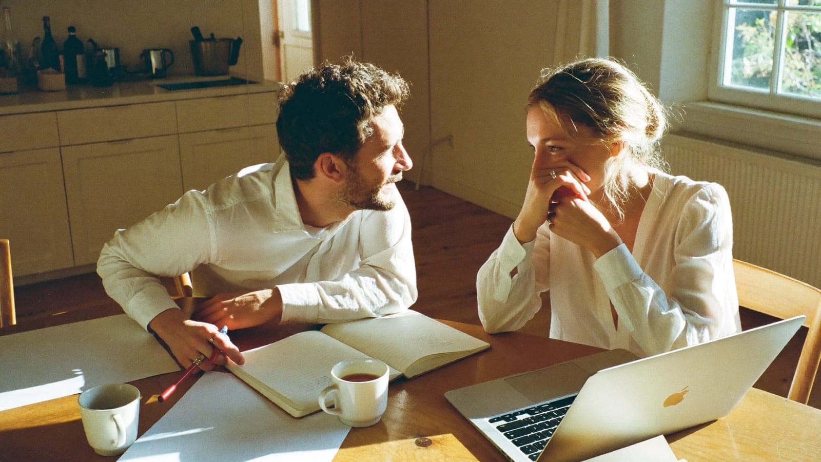 Een verloofd stel plant aan de keukentafel de bruiloft met een notitieboek en een laptop