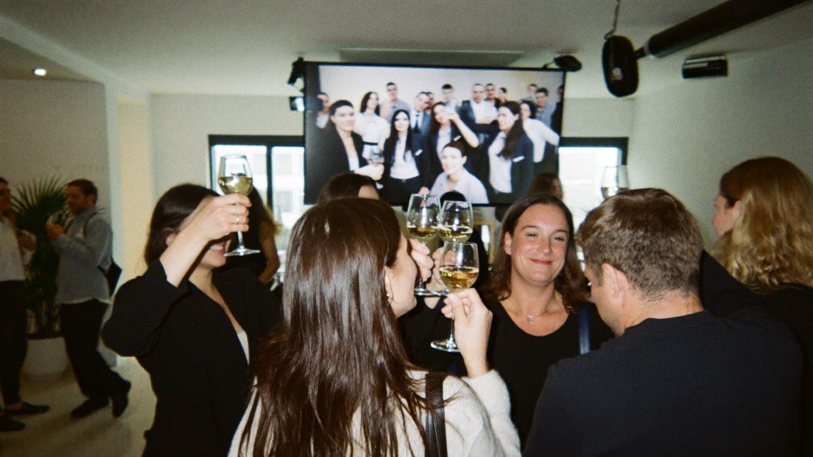 Collega's heffen het glas op de nieuwjaarsborrel, met een fotoslideshow op het scherm achter hen