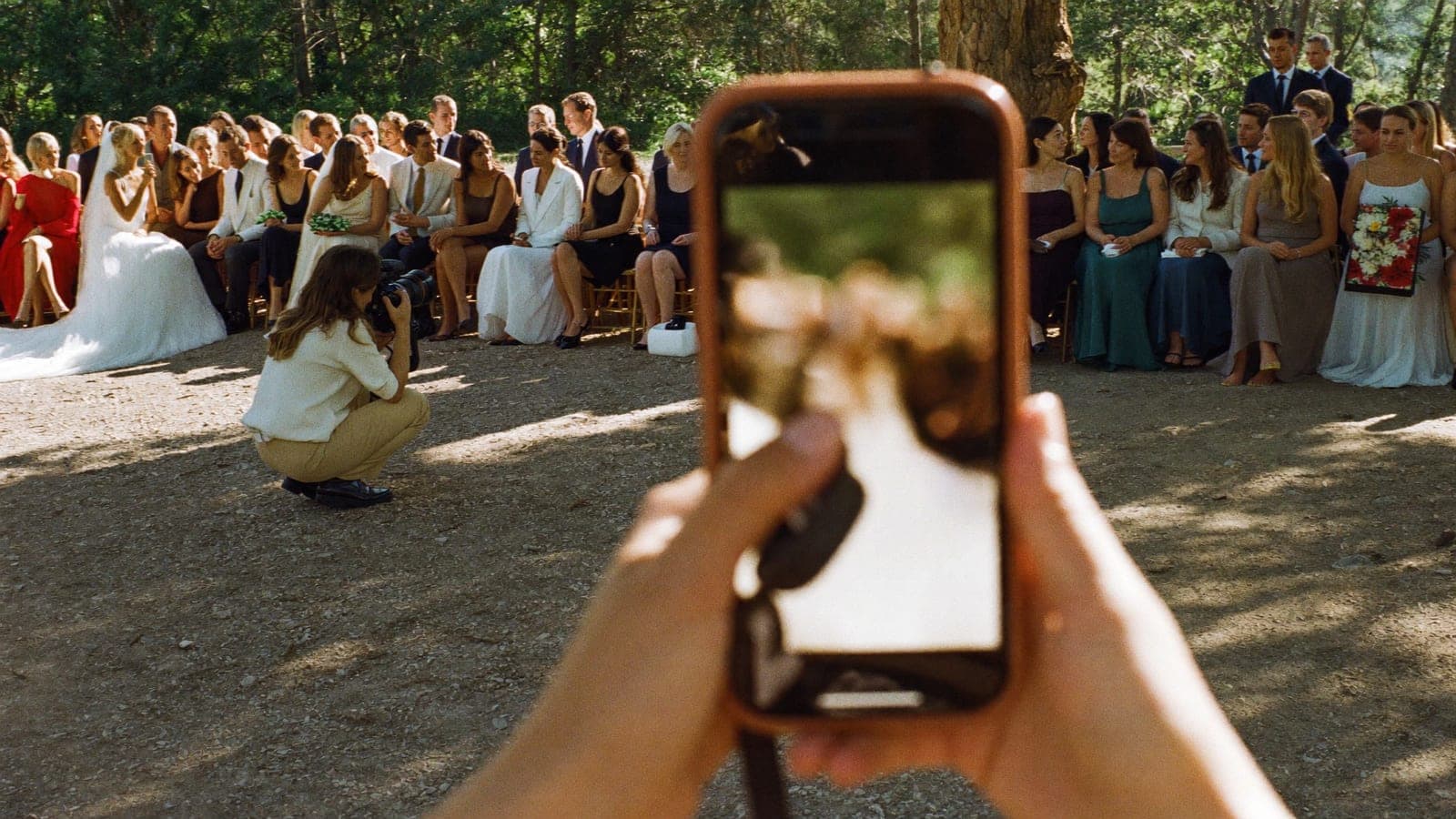 Een gast fotografeert met haar telefoon hoe de fotograaf het bruidspaar vastlegt bij de ceremonie