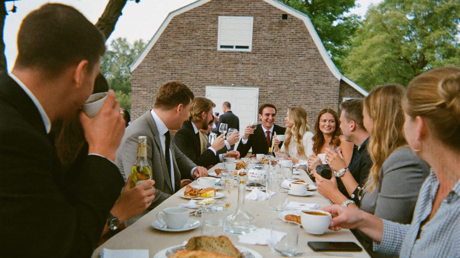 Vrienden en het bruidspaar aan een lange brunchtafel buiten, de dag na de bruiloft