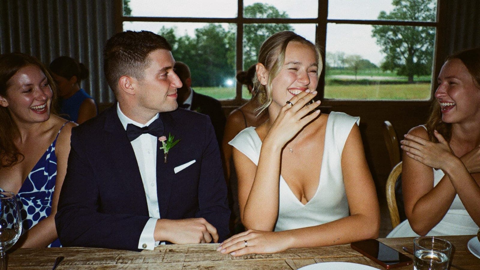 Gasten lachen aan de dinertafel, een telefoon ligt omgekeerd naast een glas