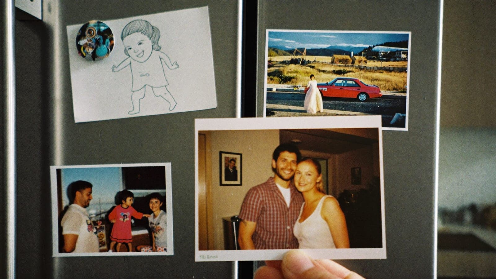 Een save-the-date-kaart hangt met een magneet op de koelkast tussen de familiefoto's