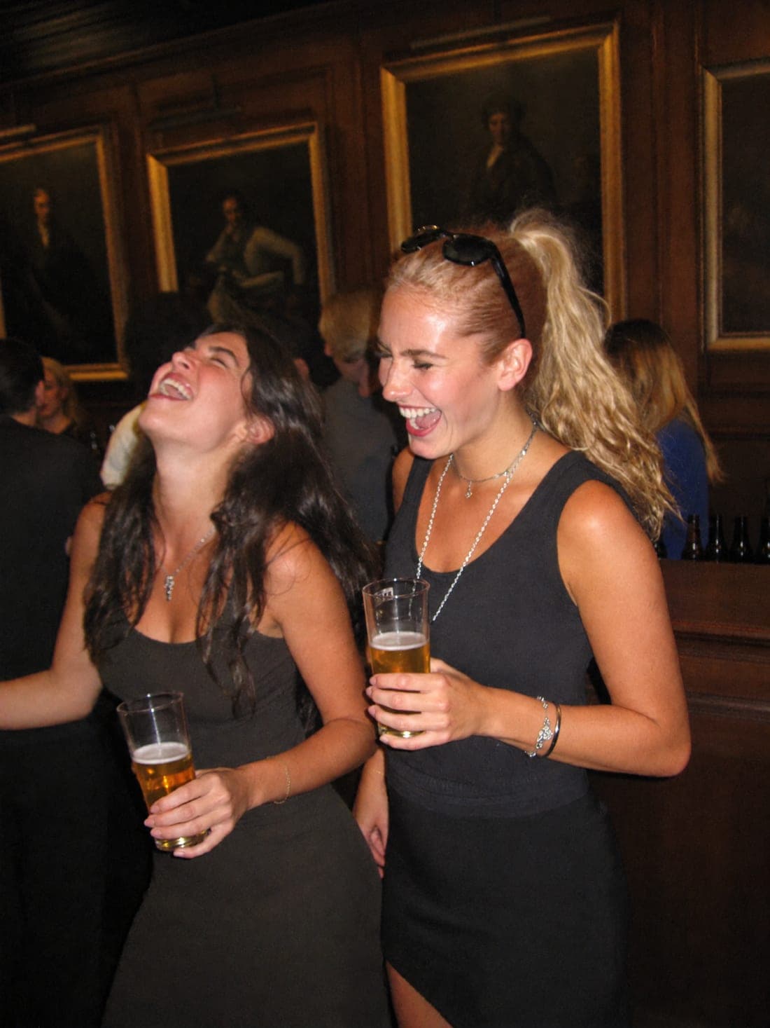 Twee leden in een lachbui aan de bar van de soos, bij de openingsborrel