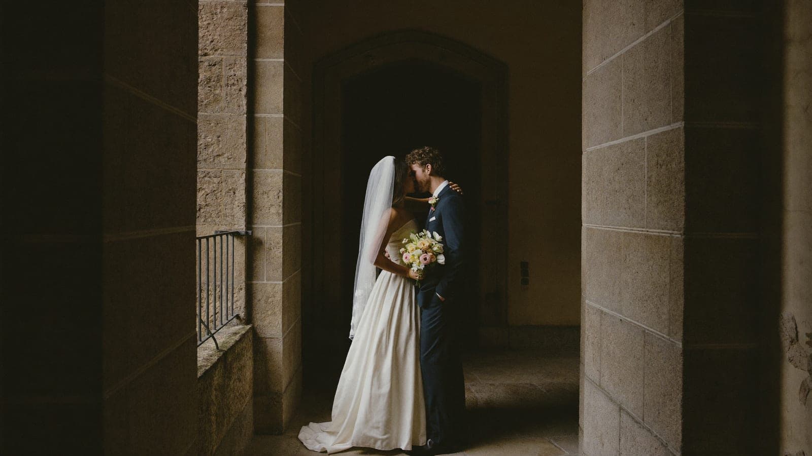 Het bruidspaar in een oude stenen doorgang, in sfeervol zijlicht