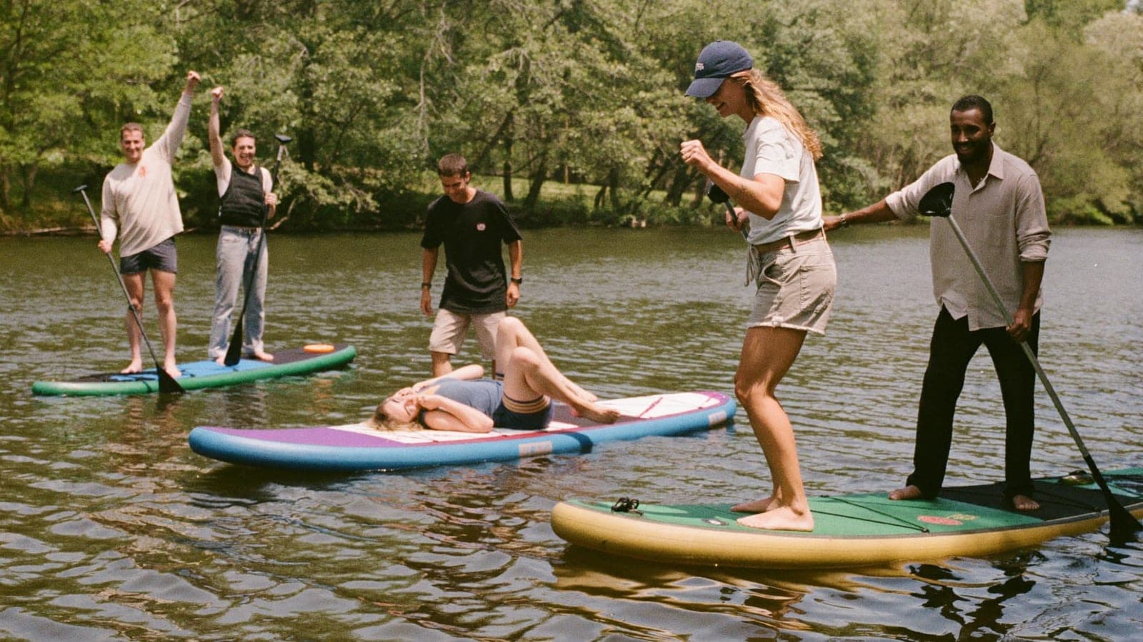 Een groep vrienden op supboards op een gracht, eentje wankelt lachend