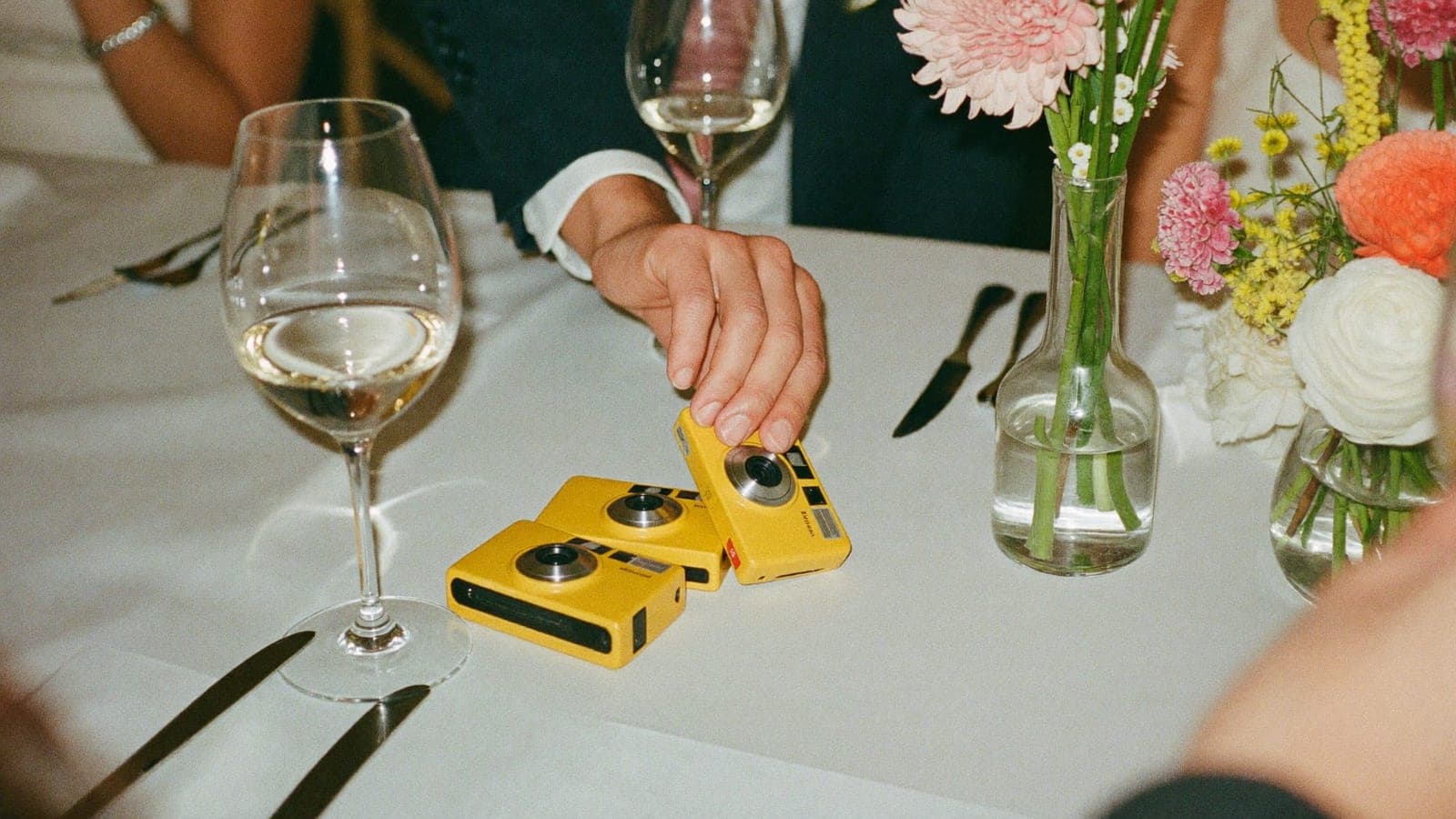 Gele wegwerpcamera's op de feesttafel tussen de wijnglazen en bloemen